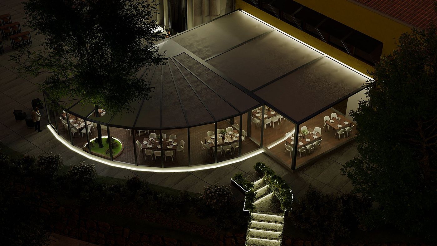 La veranda vista dall’alto, di notte: la copertura scura, l’albero al centro della sala e la scala illuminata fra le piante