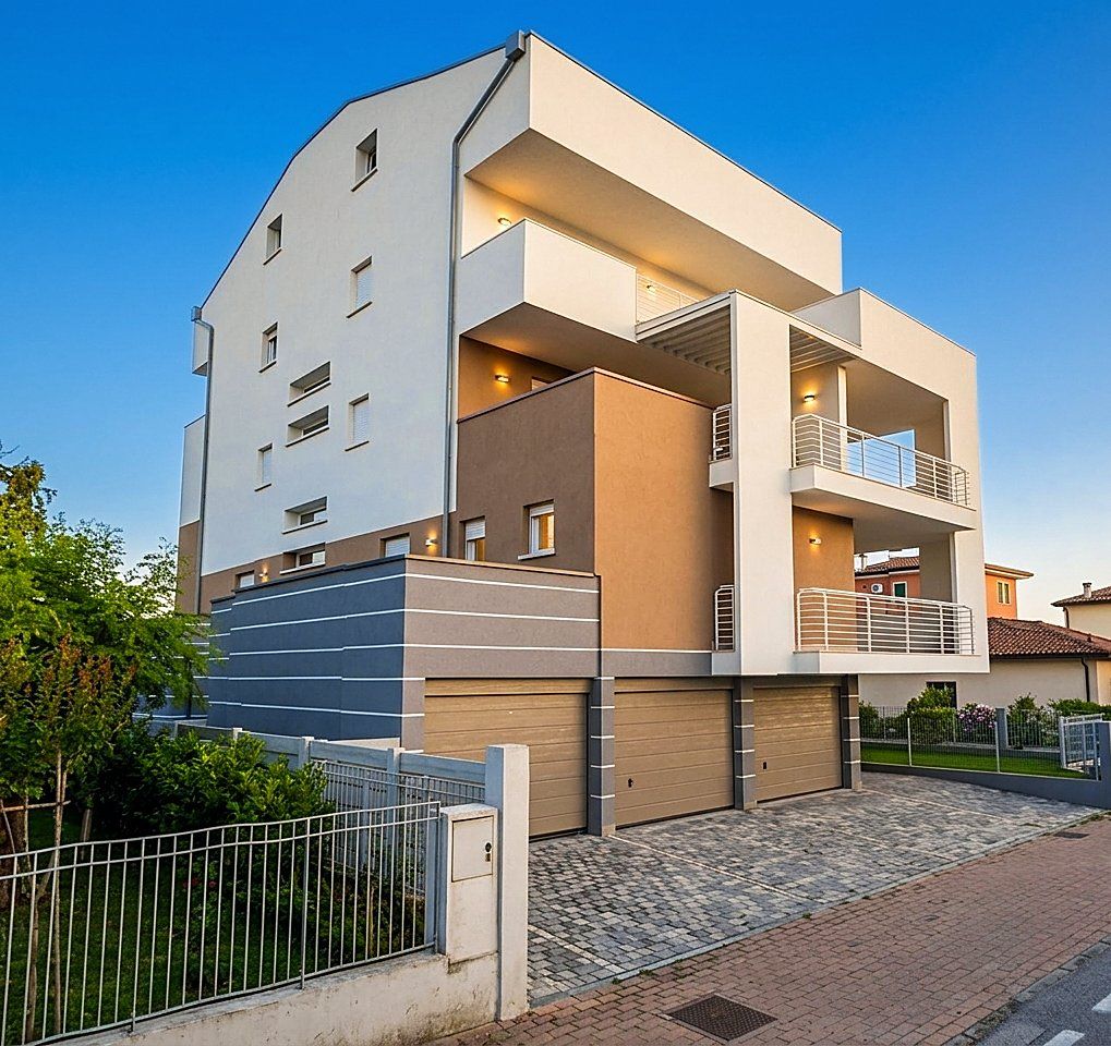 Condominio Biancon: il fronte dell'edificio all'imbrunire, con le logge, i balconi e i box auto sul piazzale